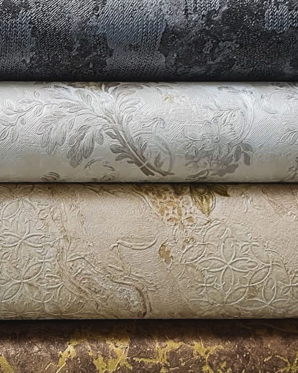 Stacked rolls of embossed wallcovering in charcoal, ivory, cream and bronze-veined finishes